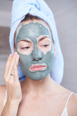 Woman applying mask moisturizing skin cream on face looking in bathroom mirror. Girl taking care of her complexion layering moisturizer. Skincare spa treatment.