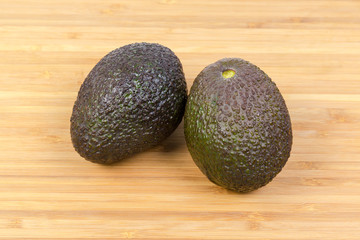 Two brown with green avocados on a wooden surface