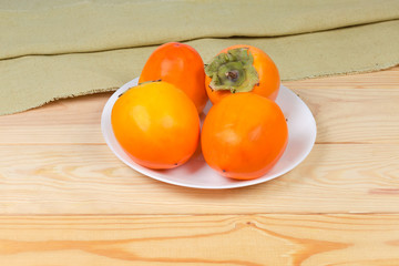 Persimmon fruits on white dish on wooden rustic table