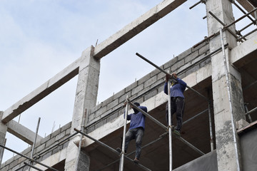 Filipino construction workers installing metal pipe scaffolds on high-rise building without protective suit.