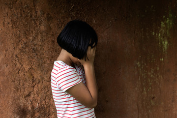 Helpless little girl against old earth brick wall,stop violence and abused children,human trafficking concept