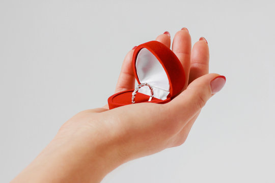 Woman hand with engagement ring in red box on gray background is
