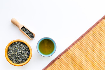 Chinese tea concept. Tea ceremony. Dry tea leaves in bowl and wooden scoop near cup of tea on white background and bamboo table mat top view copy space