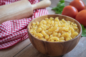 Raw macaroni pasta in wooden bowl