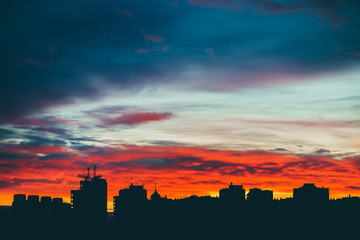 Cityscape with wonderful varicolored vivid dawn. Amazing dramatic multicolored cloudy sky above dark silhouettes of city buildings. Atmospheric background of sunrise in overcast weather. Copy space.