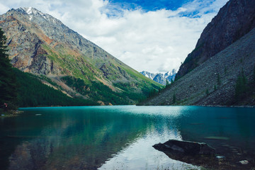 Mountain lake near huge rocky mountain with snow. Beautiful glacier. Amazing giant snowy ridge. Boulders in clean shiny water. Wonderful atmospheric landscape of majestic nature of highlands.