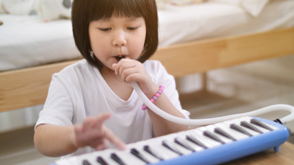 Happy little Asian girl playing melodica blow organ