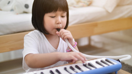 Happy little Asian girl playing melodica blow organ