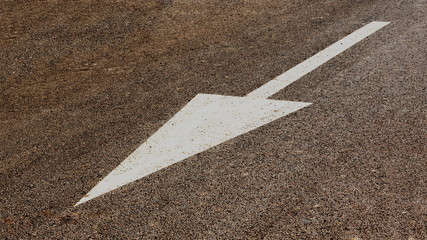 White diagonal arrow of paint on grey asphalt.