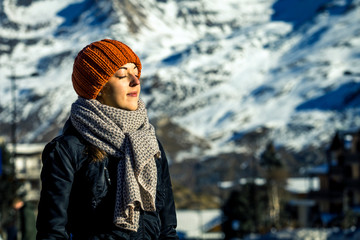 Portrait of young woman in black jacket and orange hat, sitting on the sunny day in skiing resort Tignes, France. Soft focus.