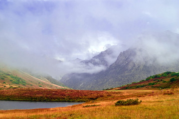 misty mountain valley with lush autumn vegetation and small lake, sheltered by low clouds