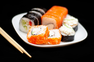 rolls with rice and fish on a white plate with wooden sticks on a black background