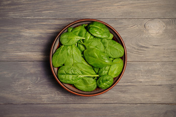 Green baby spinach leaves in  bowl on rustic wood table. Top view.
