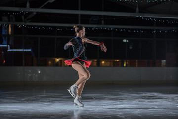 A young ice skater is finishing her spin on the ice. She is having a show.