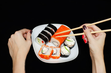 rolls with rice and fish on a white plate with wooden sticks on a black background