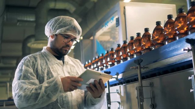 Male worker types on a tablet near conveyor with bottles, close up.