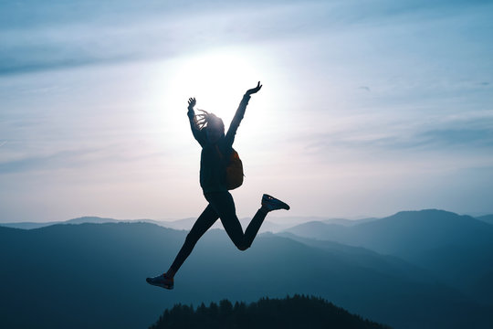 silhouette of Young woman jumping and enjoying life on mountain on sunset sky and mountains background