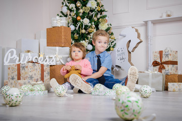 Boy and girl in the studio with a Christmas interior. Little Brother and Sister at Christmas. Waiting for children to give presents
