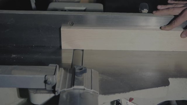 carpenter planes a piece of wood on a jointer