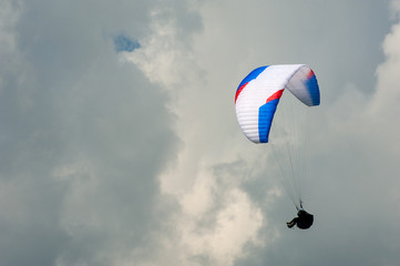 Alone paraglider flying in the blue sky against the background of clouds. Paragliding in the sky on a sunny day.