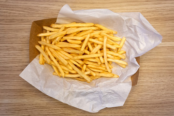 Fench fries on white paper on take away paper tray isolated on wooden table from above.