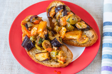 Caponata siciliana on a plate with toast close-up, top view