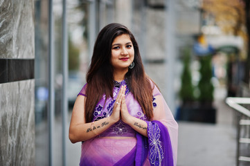 Fototapeta premium Indian hindu girl at traditional violet saree posed at street and shows namaste tatooed hands sign.