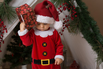 Adorable little toddler baby boy dressed in canta claus costume, playing at home in front of...