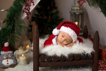 Adorable little toddler baby boy dressed in canta claus costume, sleeping in baby bed in front of crhistmas teepee