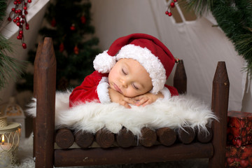 Fototapeta na wymiar Adorable little toddler baby boy dressed in canta claus costume, sleeping in baby bed in front of crhistmas teepee