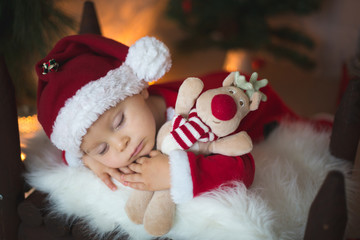 Adorable little toddler baby boy dressed in canta claus costume, sleeping in baby bed in front of crhistmas teepee
