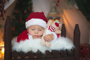 Adorable little toddler baby boy dressed in canta claus costume, sleeping in baby bed in front of...