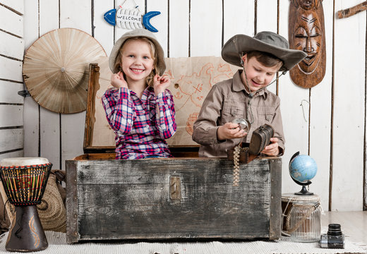 Smiling little boy and girl with jewelry while sitting in big old chest