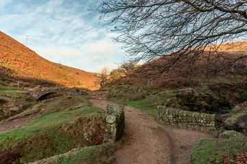 An autumnal waterfall and stone packhorse bridge at Three Shires Head in the Peak District.