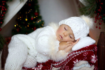 Adorable little toddler baby boy dressed in canta claus costume, sleeping in baby bed in front of...