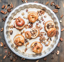 baked apples with honey and nuts on a baking tray, all ingredients are laid around on a wooden rustic background