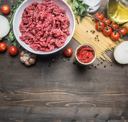 bolognese pasta cooking concept, raw minced meat, tomato paste, cherry tomatoes, pasta, onion, garlic, herbs and herbs, oil and hot leaves on a rustic wooden background, place for text