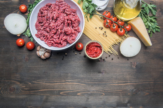 bolognese pasta cooking concept, raw minced meat, tomato paste, cherry tomatoes, pasta, onion, garlic, herbs and herbs, oil and hot leaves on a rustic wooden background, place for text