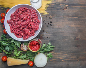 bolognese pasta cooking concept, raw minced meat, tomato paste, cherry tomatoes, pasta, parmesan, onions, garlic, herbs and herbs, oil and cold leaves on a rustic wooden background, place for text