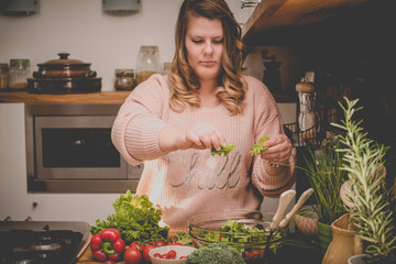 Beautiful plus size woman is making fresh salad in the kitchen