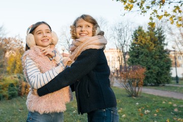 Outdoor portrait of two little girls best friends, smiling girls hugging each other watching the sunset, sunny autumn winter park, golden hour
