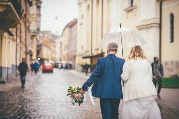 Fototapeta premium Back view of bride and groom under the clear umbrella