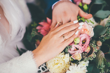 Bride and groom hold their hands on the bouquet