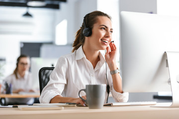 Emotional business woman in office callcenter working with computer wearing headphones.