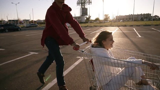 Young millennials people racing with shopping carts - Happy crazy friends having fun with trolleys in car park. Girls in the corts giving each other high five. Youth lifestyle, friendship and party
