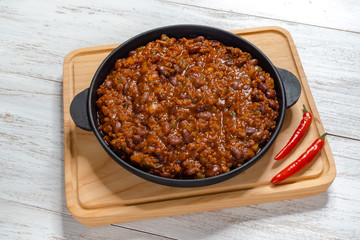 Mexican chili. Chili con carne in frying pan on white wooden background. 
