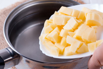 Hand adds raw potato pieces in boiling water