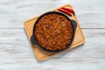 Mexican chili. Chili con carne in frying pan on white wooden background. 
