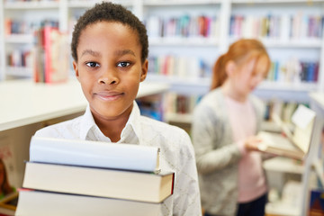 Schüler in Grundschüle trägt Bücher aus Bibliothek - obrazy, fototapety, plakaty