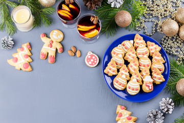 Tasty Christmas cookies, hot mulled wine and decorations with Christmas tree and lights on black background.